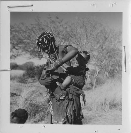 Woman from /Ti!kay's group standing and carrying her baby, tying her kaross