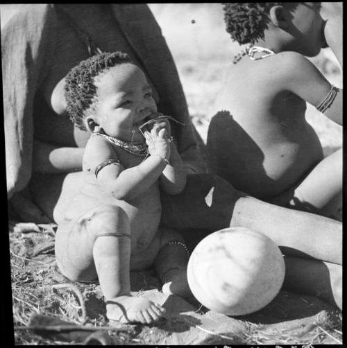 Baby (child of ≠Gao, leader of Band 10, and Bau, his first wife) sitting next to an ostrich eggshell