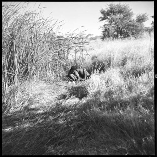 Two boys filling ostrich egg shells with water at a waterhole, distant view