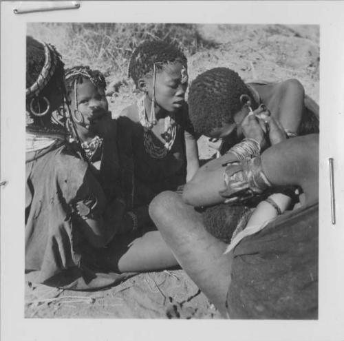 Group of women and girls sitting, with one woman fixing another woman's earring