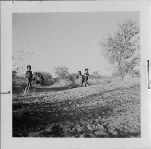 /Gaishay and "Little Gao" playing the stick-throwing game, standing on an ant-hill, with another boy standing near them