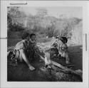 Woman and a girl sitting by a fire, with a child standing next to the woman