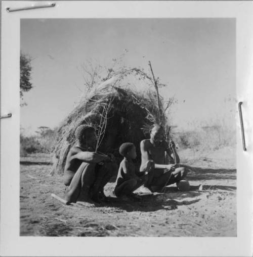 "/Qui Navel" making a bow, sitting in front of a skerm with "Old Demi" (leader of Band 6), "/Qui Navel" and !Naishi (/Qui's son)