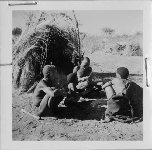 "/Qui Navel" making a bow, sitting in front of a skerm with "Old Demi" (leader of Band 6), "/Qui Navel," !Naishi (/Qui's son) and an unidentified person