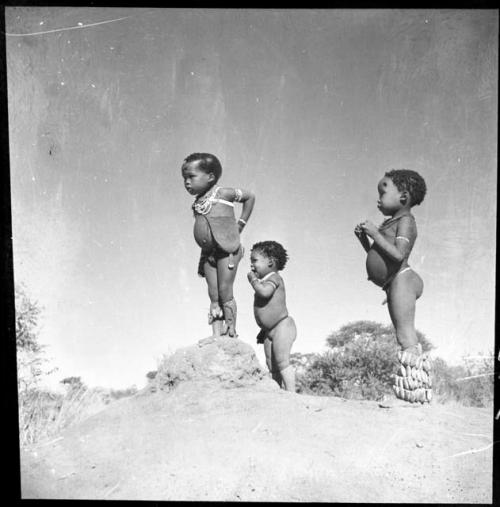 /Gaishay (son of "Gao Medicine" and Di!ai), Bau (daughter of "Crooked /Qui"), and "Little ≠Gao" (son of "/Qui Navel") standing on an ant hill