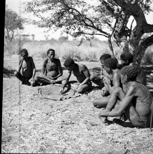 Man reading an oracle disk, and a group of men sitting and watching him