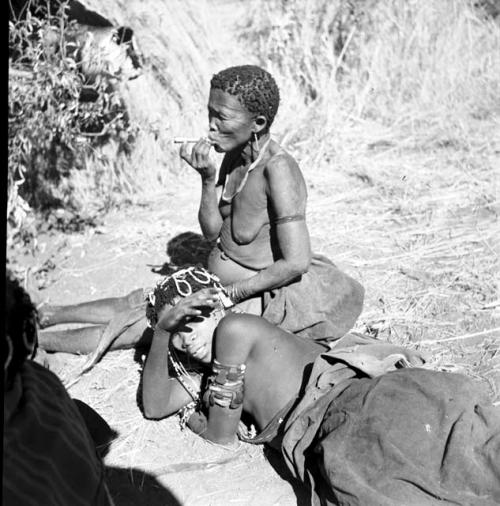 Woman smoking a pipe, with another woman wearing ornaments and upper arm bracelets lying beside her