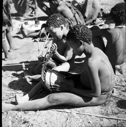 Two boys sitting, one playing a //guashi and one tuning one