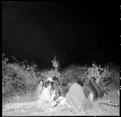 Group of people sitting with Lorna Marshall at night, illuminated by flashlight