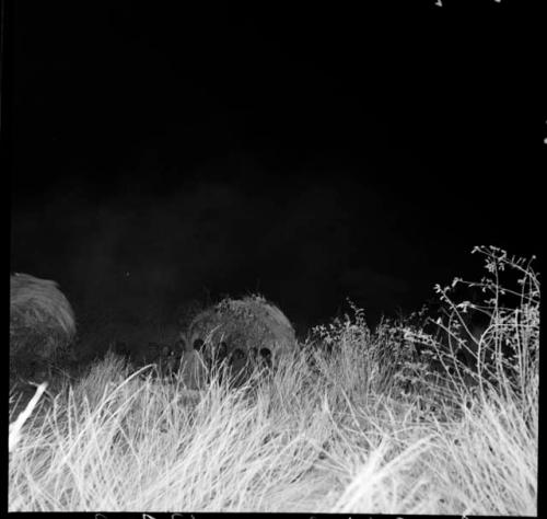 Group of people sitting in front of a skerm at night, illuminated by flashlight, distant view