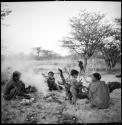 ≠Toma sitting with a group of people by a smoking fire