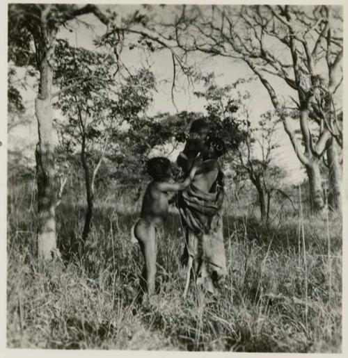 Woman lifting a baby, standing with a boy in the mangetti forest