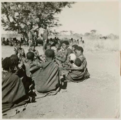 /Naoka giving a drink of water her child while sitting with women in the dance circle