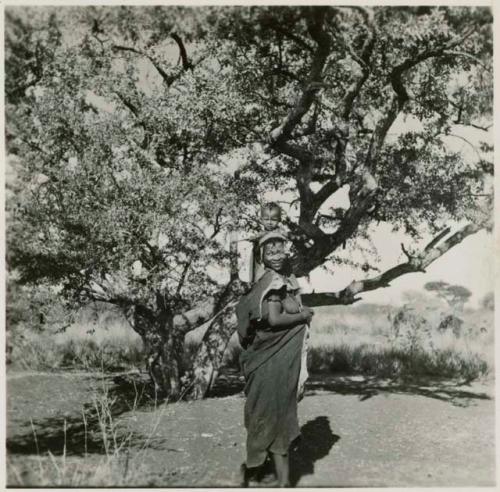 /Goishay (wife of ≠Gao) standing, holding a child on her shoulders