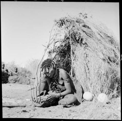 Khuan//a (daughter of !Naishi, headman of Band 5, and //Khuga) sitting in front of a skerm, playing a //guashi