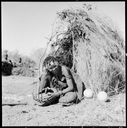 Khuan//a (daughter of !Naishi, headman of Band 5, and //Khuga) sitting in front of a skerm, playing a //guashi