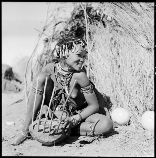 Khuan//a (daughter of !Naishi, headman of Band 5, and //Khuga) sitting in front of a skerm, playing a //guashi