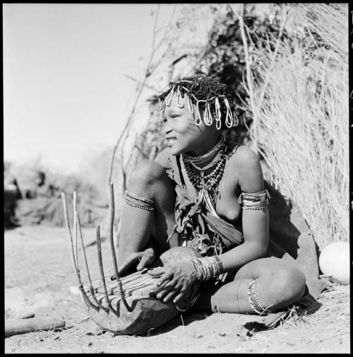 Khuan//a (daughter of !Naishi, headman of Band 5, and //Khuga) sitting in front of a skerm, playing a //guashi