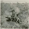 Woman digging up a root, with a baby tied to her back