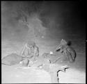 Woman holding a baby, sitting with a man next to a fire at night