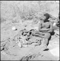 "Old Gau" of Band 1 sitting, with a kaross, dance rattles and an ostrich eggshell on the ground next to him