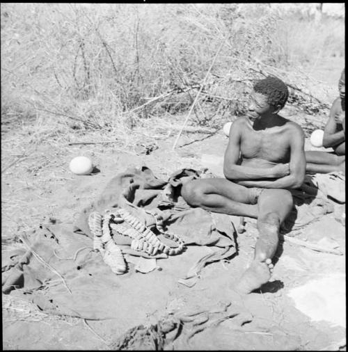 "Old Gau" of Band 1 sitting, with a kaross, dance rattles and an ostrich eggshell on the ground next to him