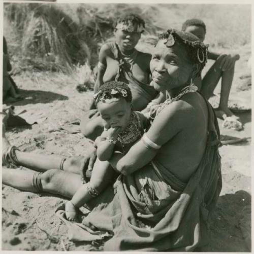 Woman from /Ti!kay's group holding her child, sitting with //Kushay from Band 1 behind her