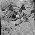 Woman from /Ti!kay's group holding her child, sitting with a group of women