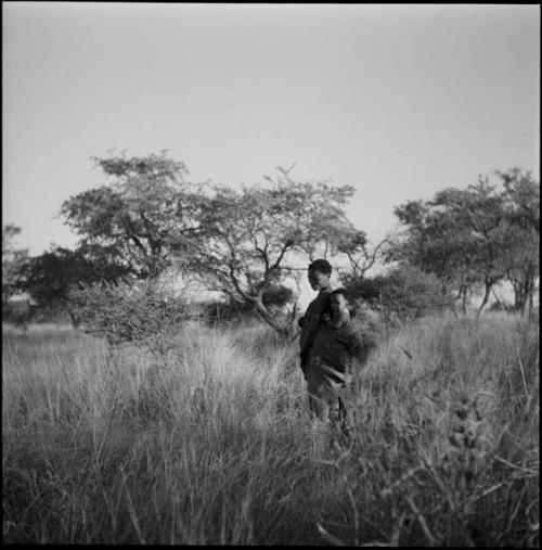 Woman with a child on her back walking in the grass