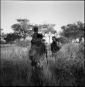 Woman with a child on her shoulders, walking with a woman carrying a load of grass and a baby on her back