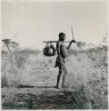 Man carrying an assegai and a net full of ostrich egg shells hung on his carrying stick