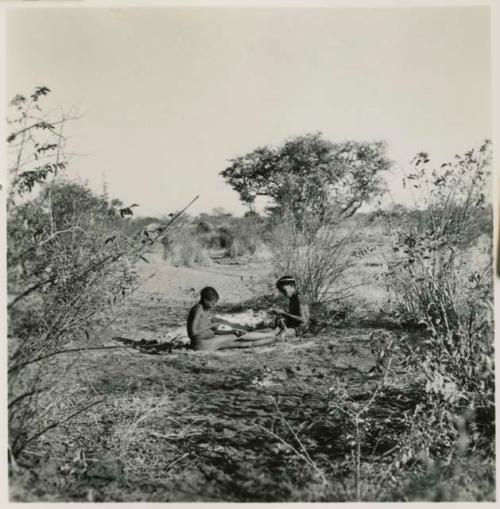 Two boys sitting on the ground making djani toys (helicopter toys)