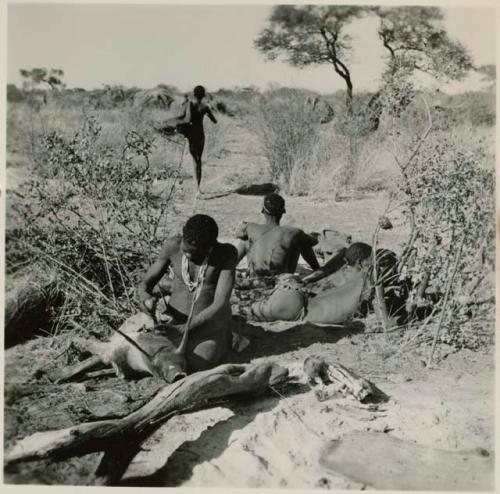 Man making a bag from wild pig skin, with a group of men sitting behind him