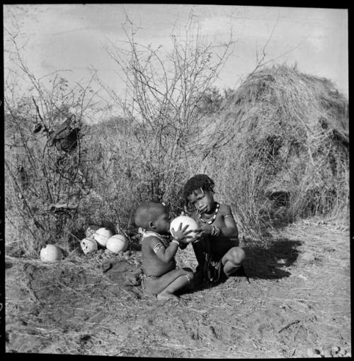 "Little N!ai" giving /Gaishay a drink from an ostrich eggshell