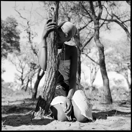 Woman wearing a dress made from a tablecloth, sitting, leaning against a tree