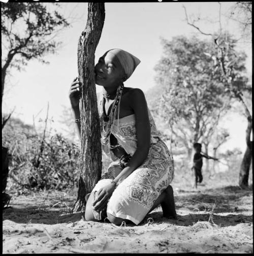 Woman wearing a dress made from a tablecloth, sitting, leaning against a tree