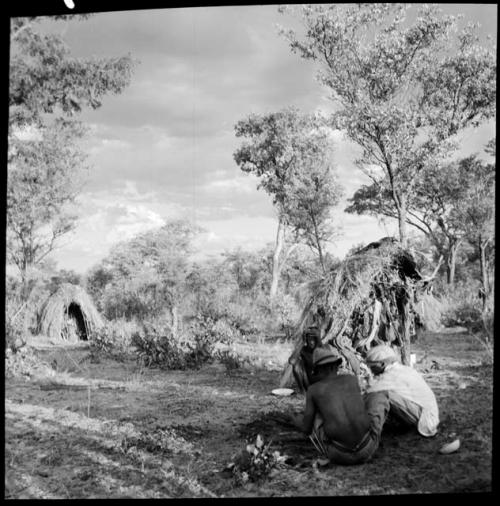 Men wearing Western clothing, sitting next to a shelter skerm, with a skerm in the background