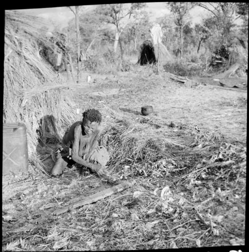 /Naoka kneeling next to a skerm, with a large pot and a jerry can on the ground near her