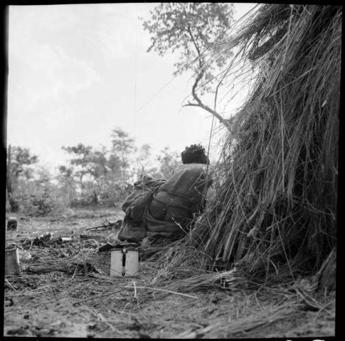 /Naoka kneeling next to a skerm, view from behind, with an enamel cup on the ground near her