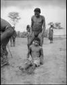 Ngani sitting on the ground, in trance, and "/Qui Navel" standing behind him in partial trance