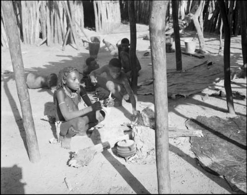 Rungiero's sister sitting beside a cooking fire, with people sitting in the background