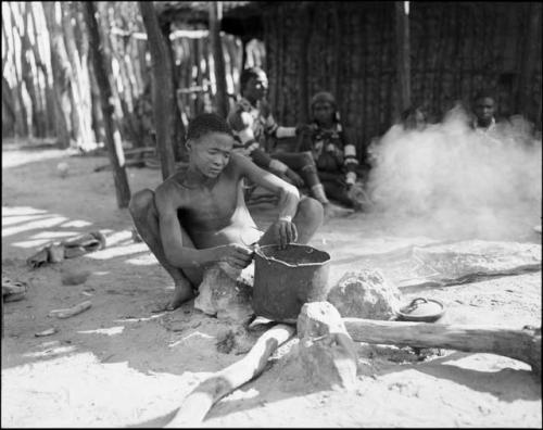 Boy putting a pot on the fire, with Makiena and her daughter-in-law and other unidentified people in the background