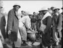 WNLA (Witwatersrand Native Labor Association) convoy cook making mealie porridge, with a group of men watching, most wearing mine helmets
