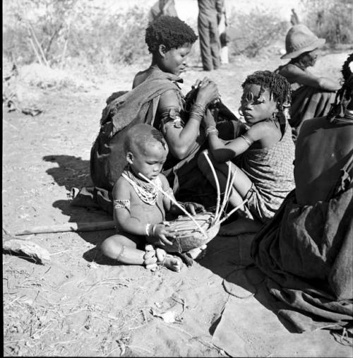 //Khuana looking for lice on her child's head, N!ai looking for lice in the child's beads, and /Gaishay (son of Gao and Di!ai) examining a //guashi