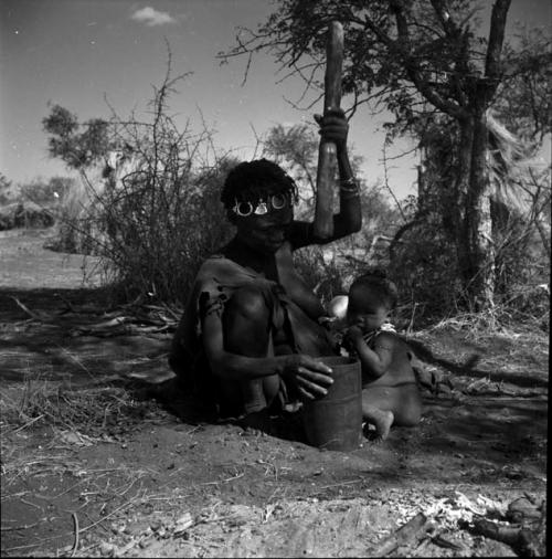 ≠Toma's sister pounding something with mortar and pestle, with her child sitting next to her