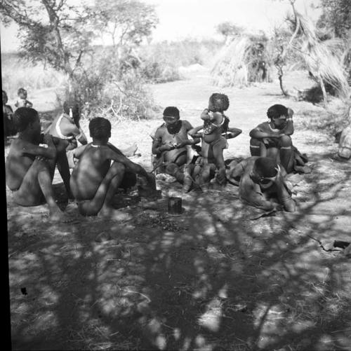 Group of women and boys sitting, including "≠Gao Lame" taking something out of a mortar