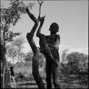 Man wrapped in a kaross standing, holding on to a small tree