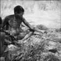 "Gao Medicine" examining his arrows which are resting against a log