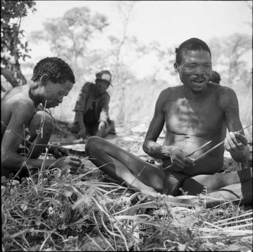 "Gao Medicine" talking, holding arrows, witting with another man working on an arrow