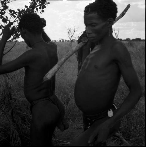 Two men standing, one holding a digging stick